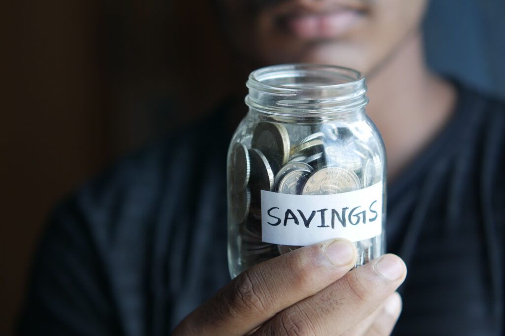 How to Create a Budget That Actually Works (and Start Saving Without Suffering) Persona sosteniendo un frasco con monedas etiquetado como ahorros